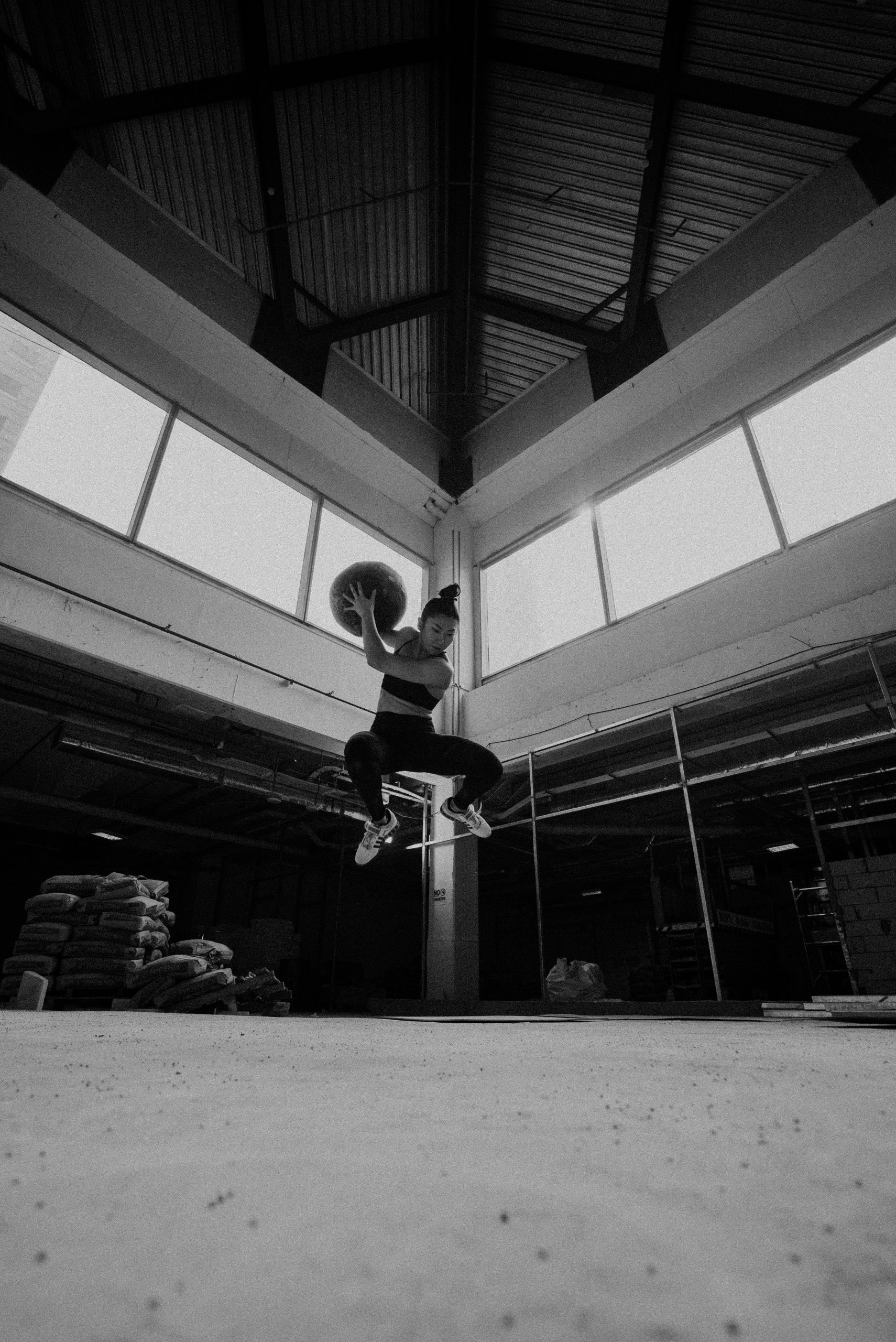 An athlete mid-air with a medicine ball in a black-and-white warehouse gym