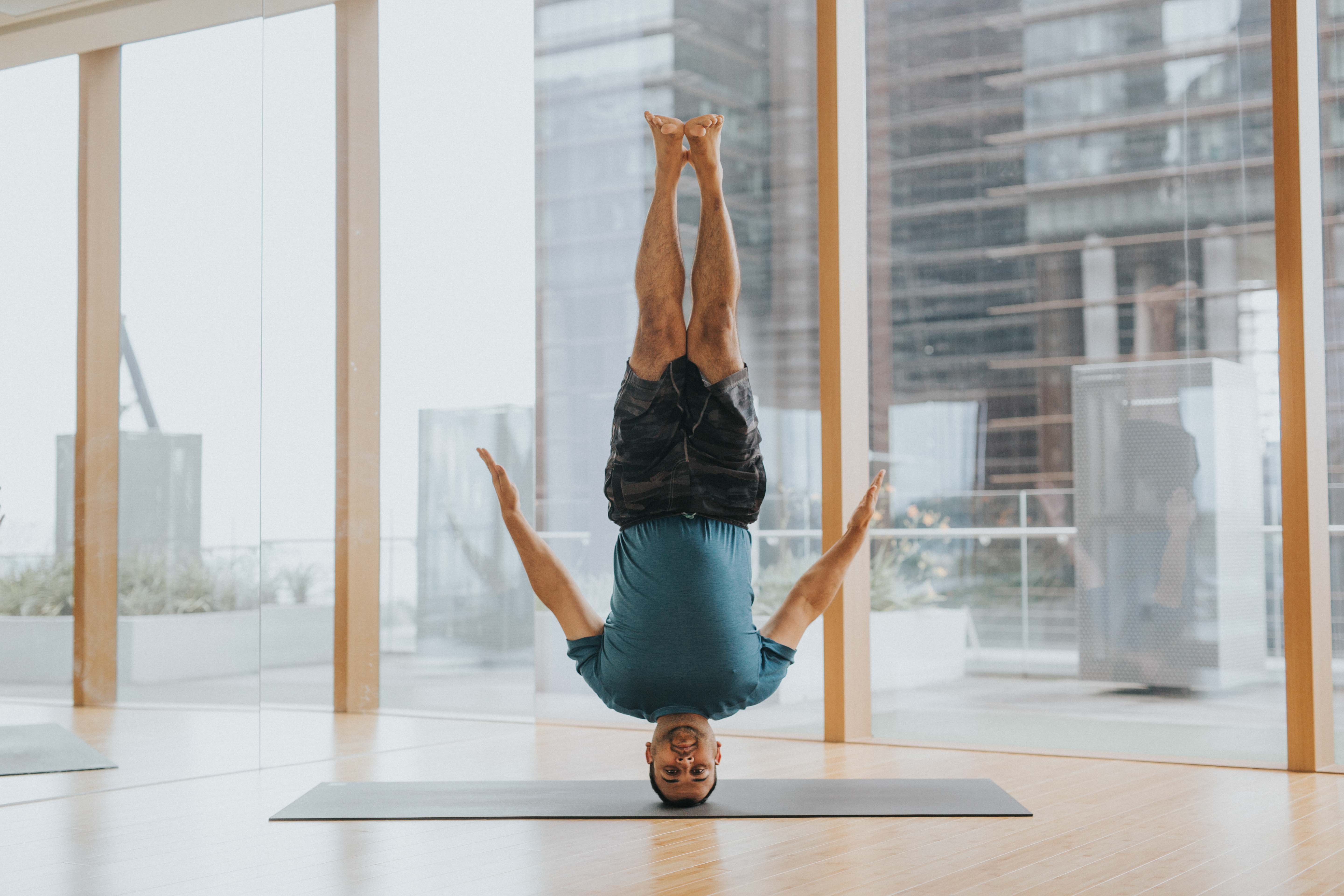 A man balancing in a headstand with arms spread in a glass-walled studio