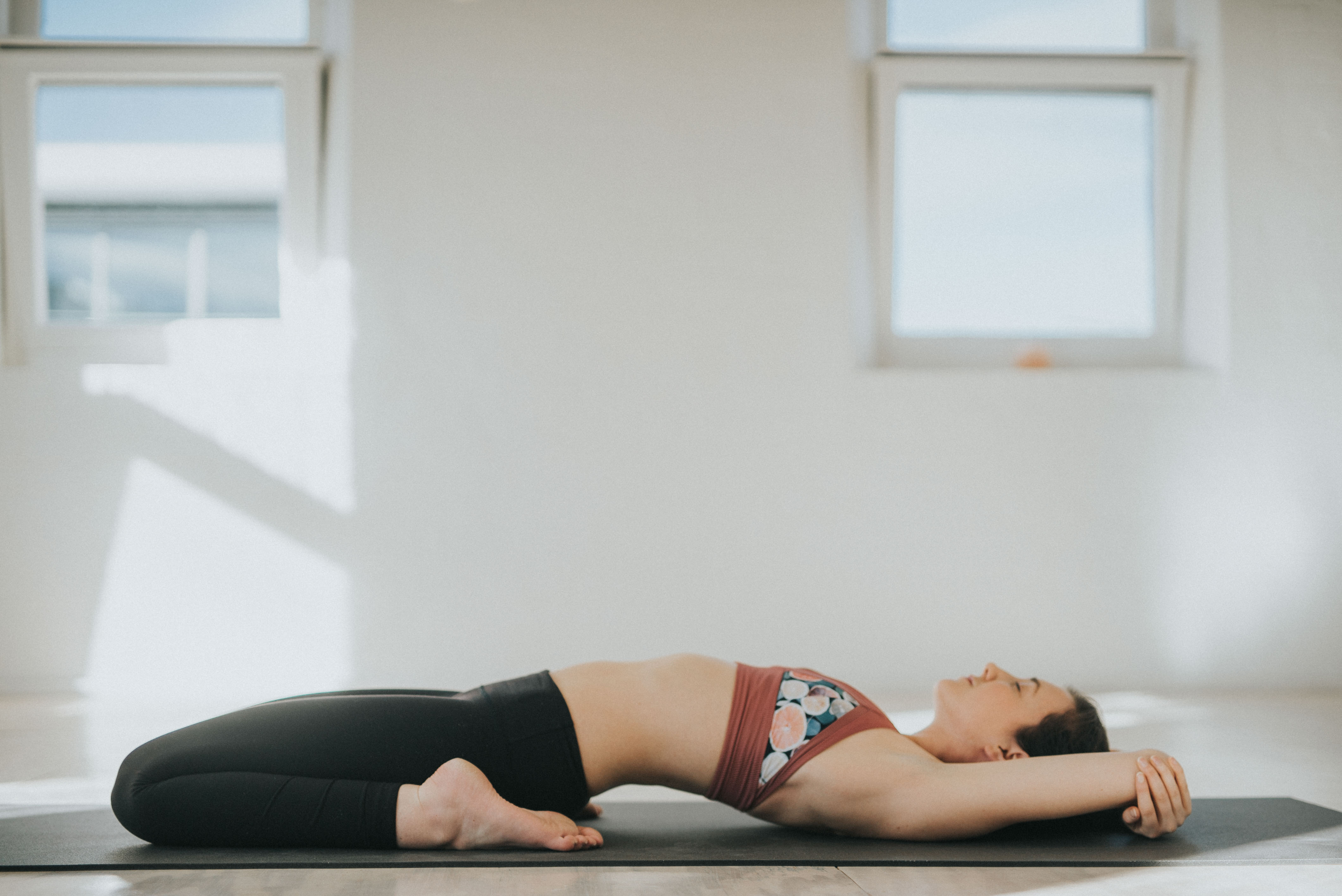 A yogi resting in a supported backbend on a mat in a bright studio