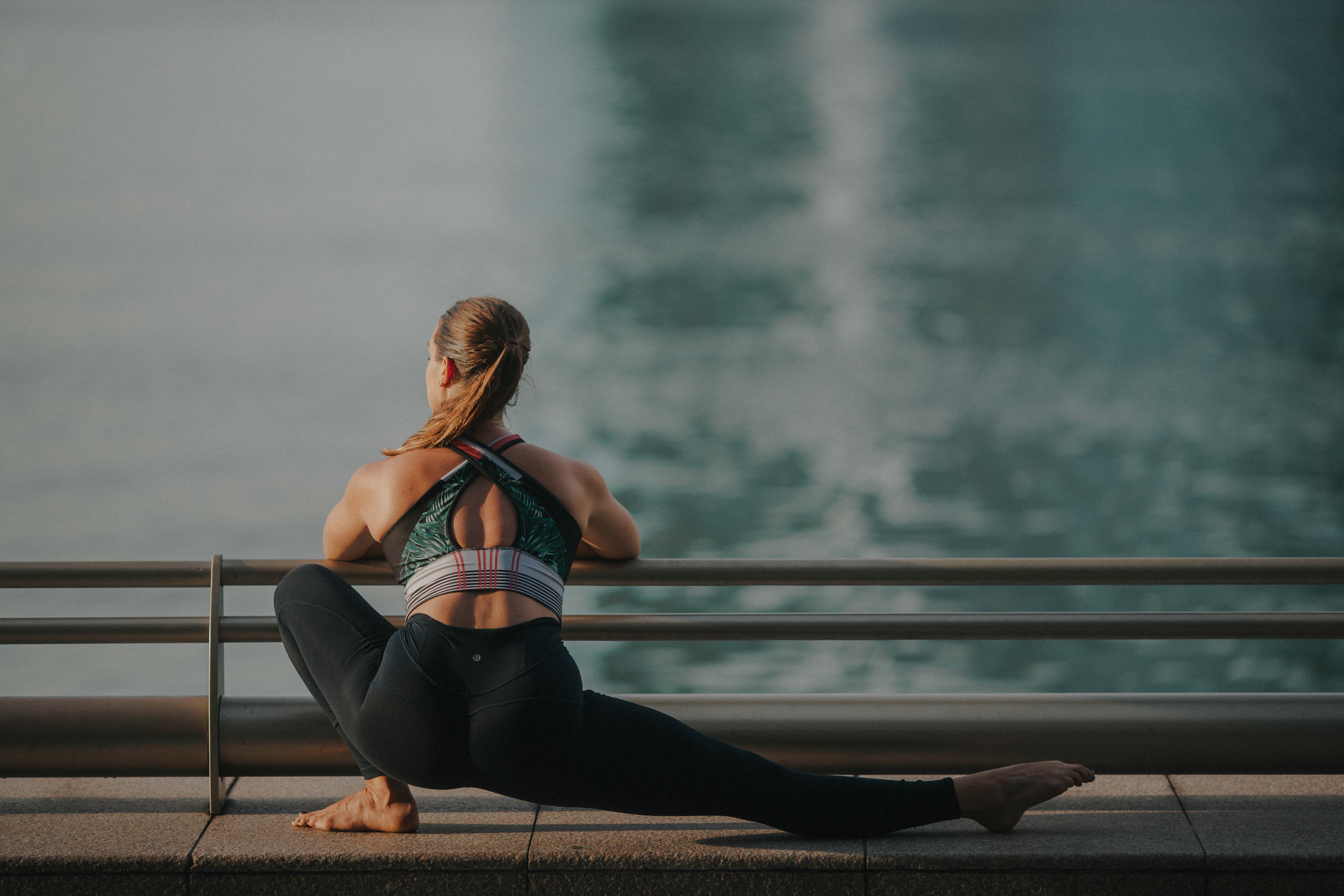 A woman stretching in a low lunge along a waterfront railing at sunrise